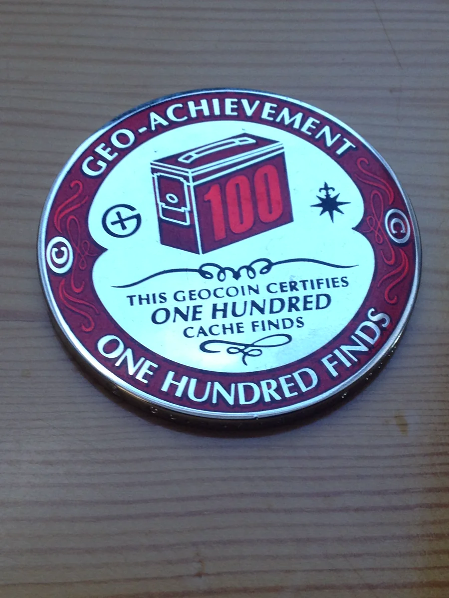 Red and white geocoin celebrating one hundred cache finds