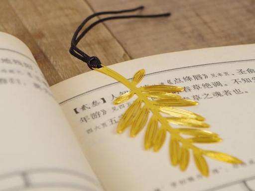 Gold-colored leaf-shaped bookmark with a dark cord resting on open book pages