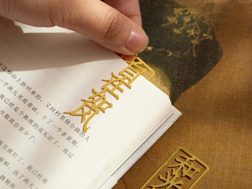 Hand holding a gold-colored Chinese-lettering bookmark over book pages