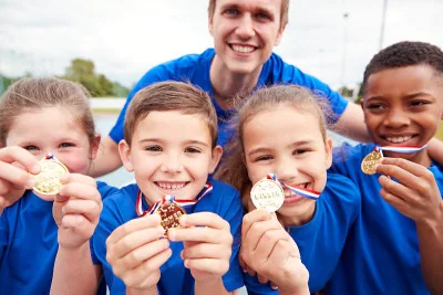 Children and coach holding sports medals after a school activity