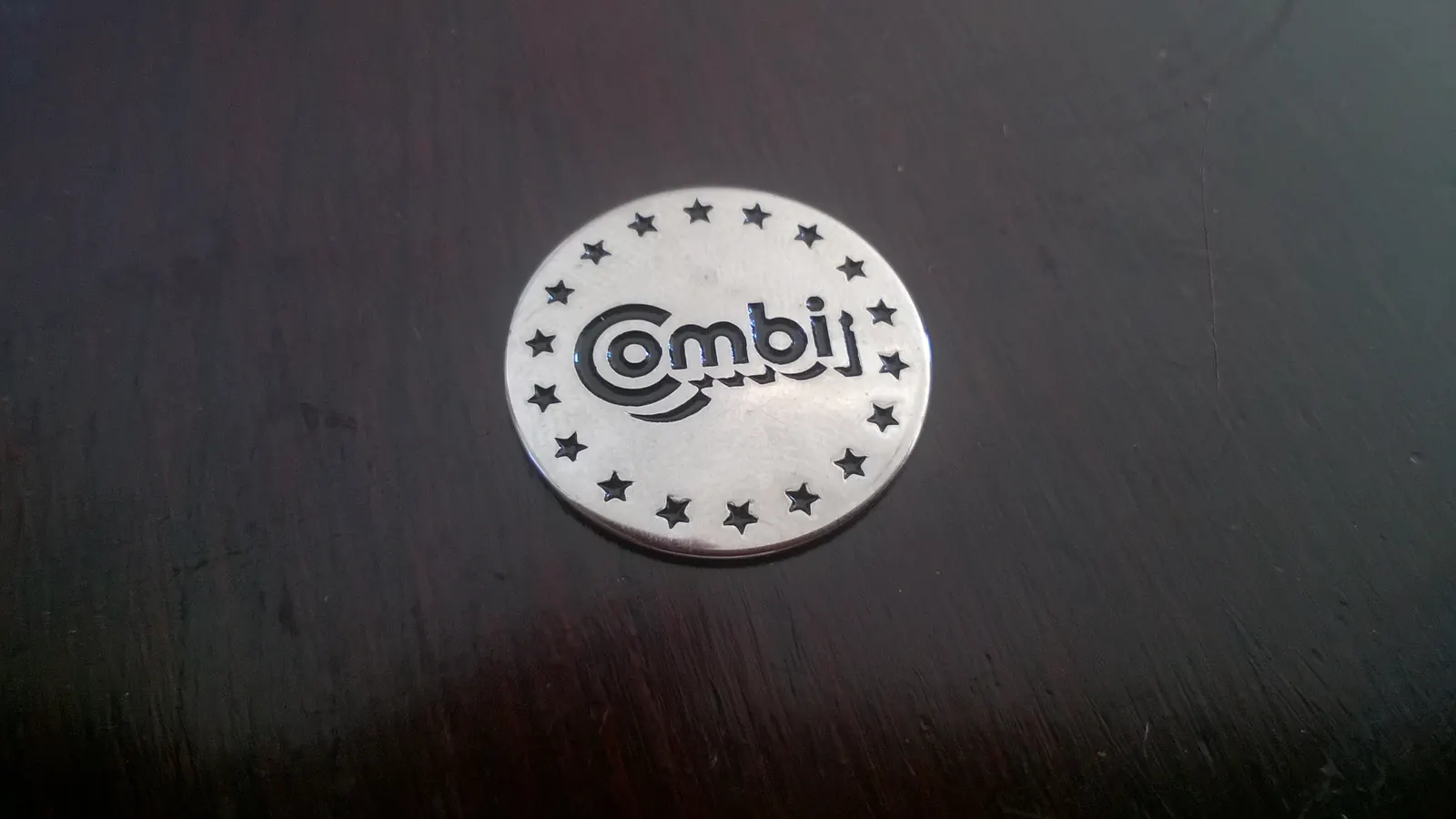 Combi branded metal shopping cart token photographed on a dark surface