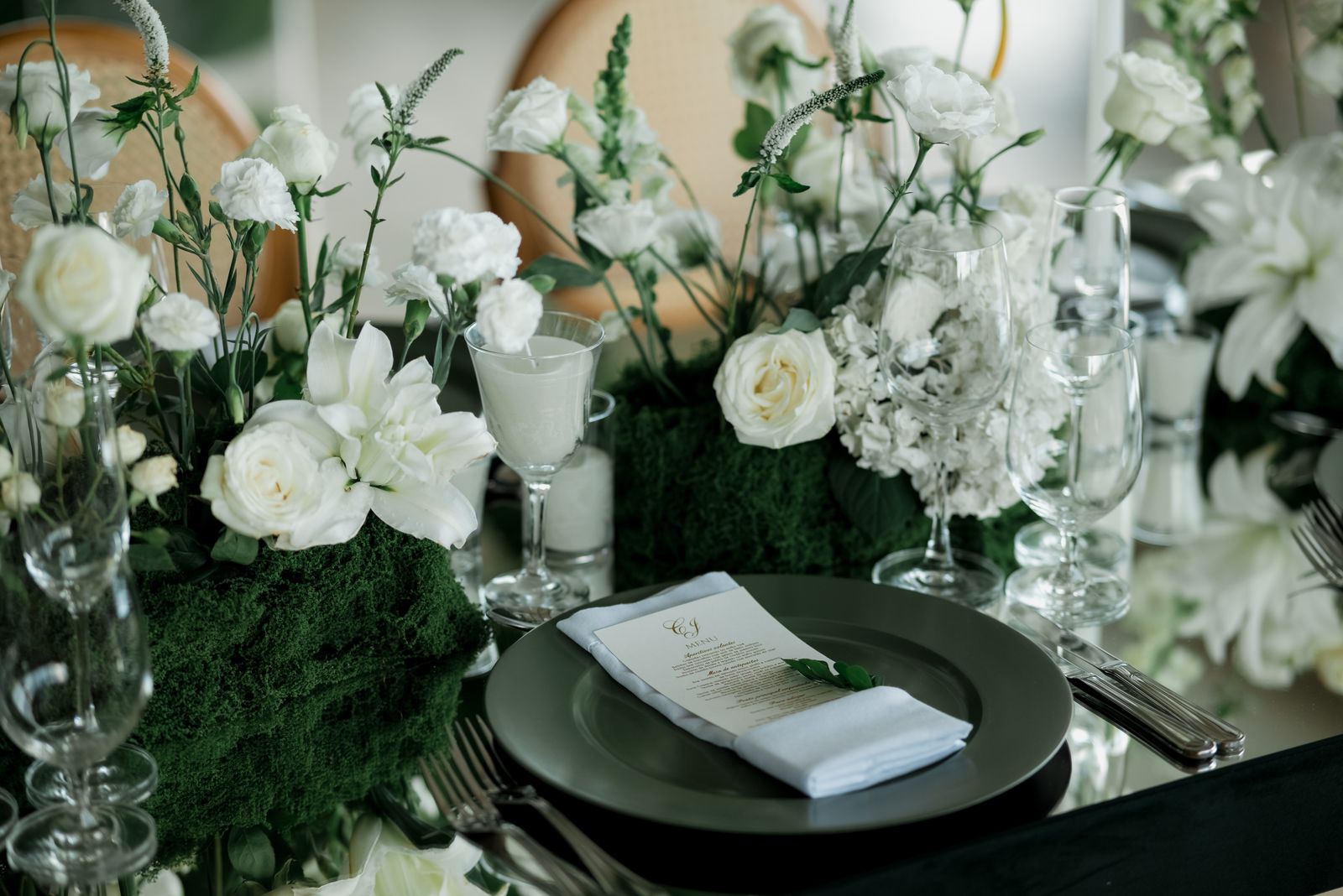 Wedding table with white flowers, greenery, glassware and a menu card on a place setting